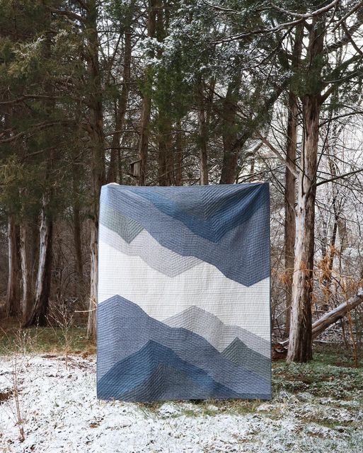 a blue and white blanket sitting on top of a snow covered ground next to trees