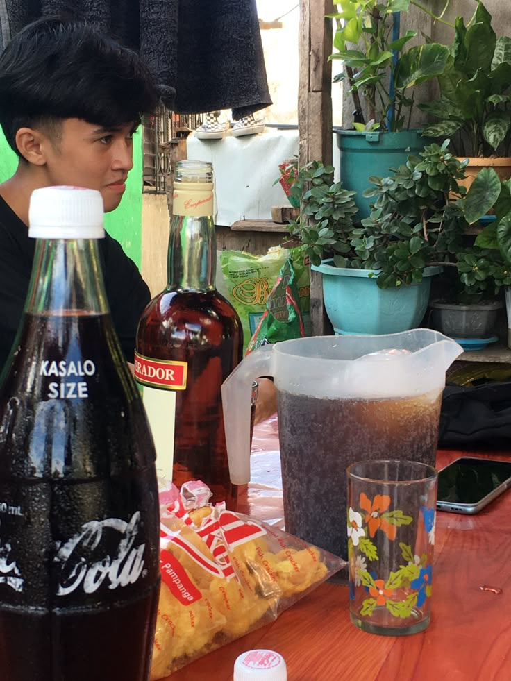 a young man standing next to a table filled with bottles and containers of sodas