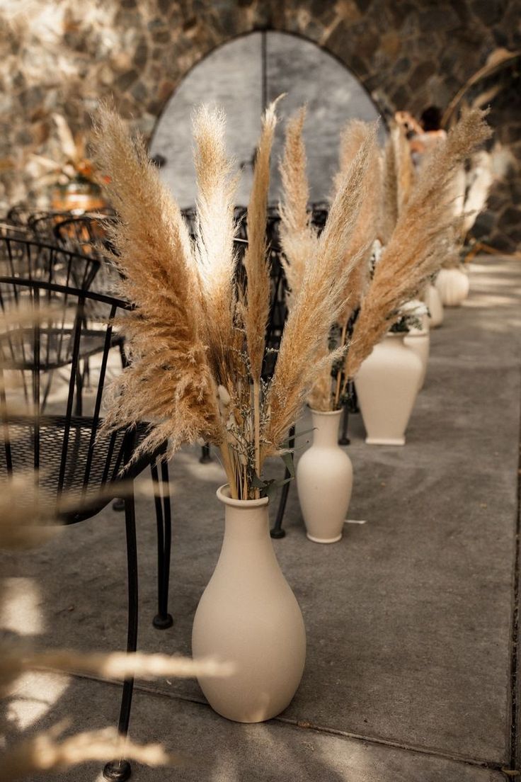 there are several vases with flowers in them on the sidewalk near chairs and tables