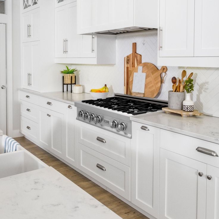 a kitchen with white cabinets and marble counter tops is seen in this image, there are cutting boards on the stove