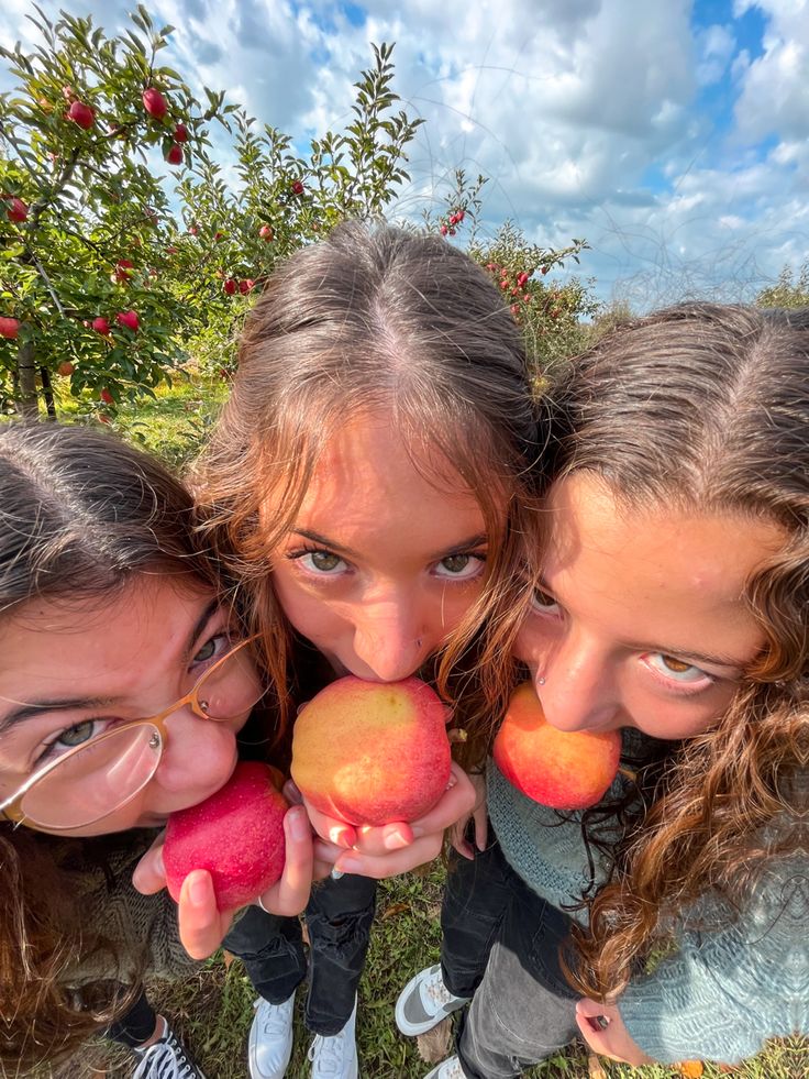 three girls are holding apples and posing for the camera with their faces close to each other