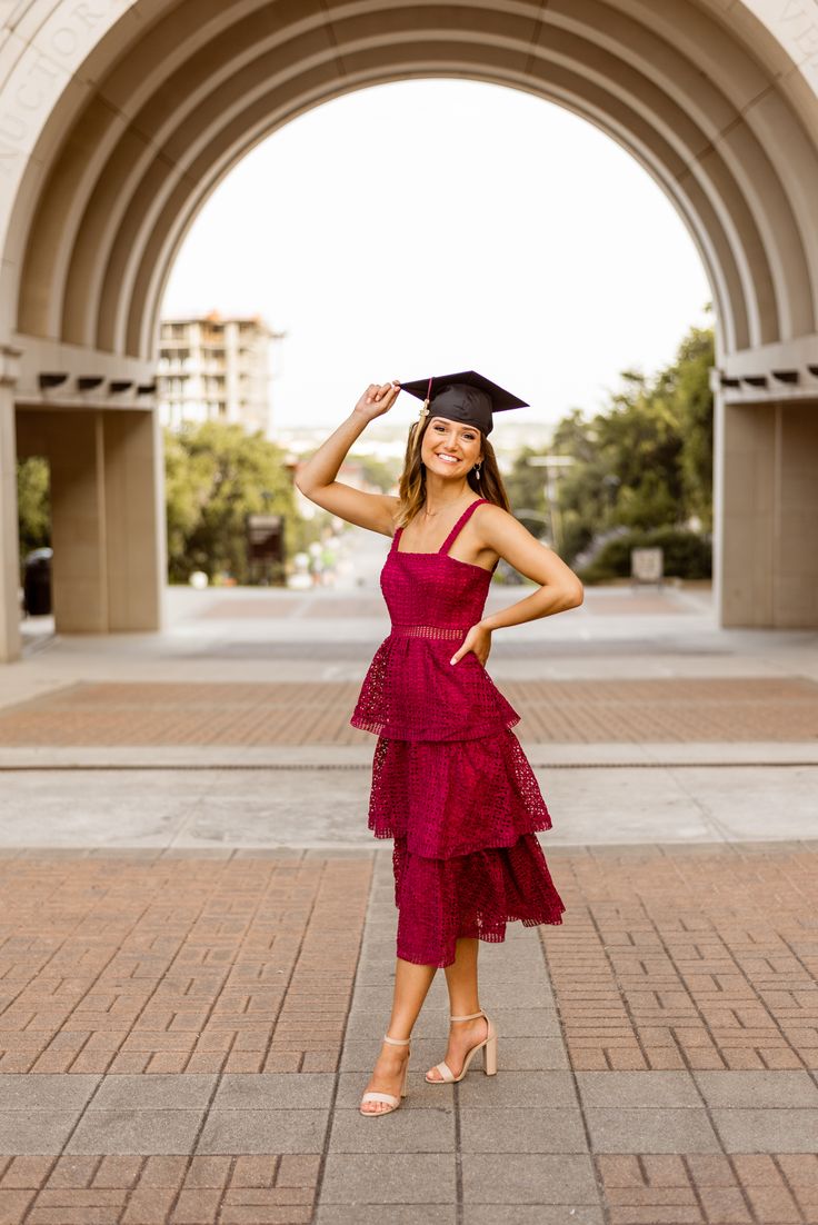 a woman wearing a graduation cap and gown posing for a photo in front of an archway