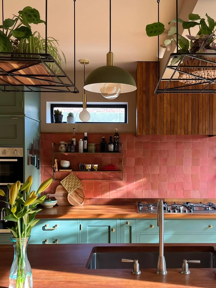 a kitchen with green cabinets and pink tile backsplashes, hanging lights over the stove