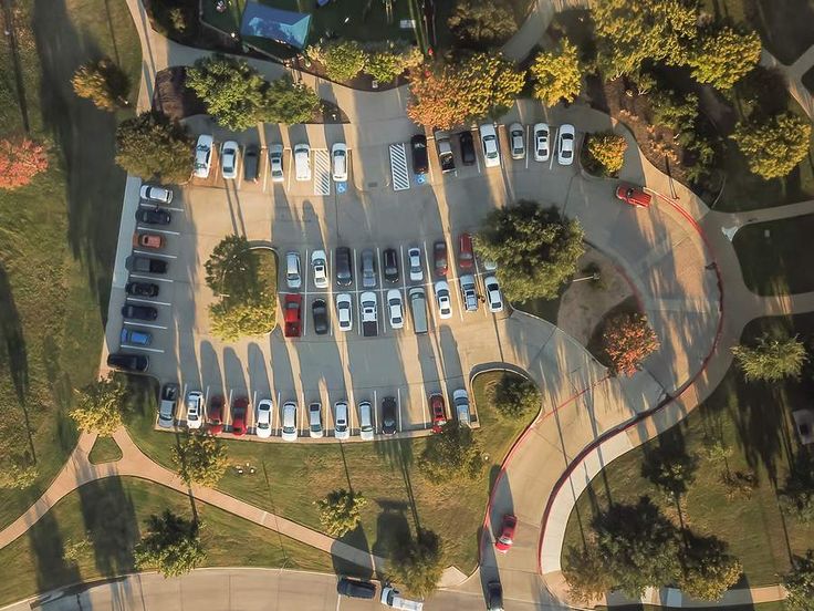 an aerial view of a parking lot with many cars parked in it and surrounded by trees