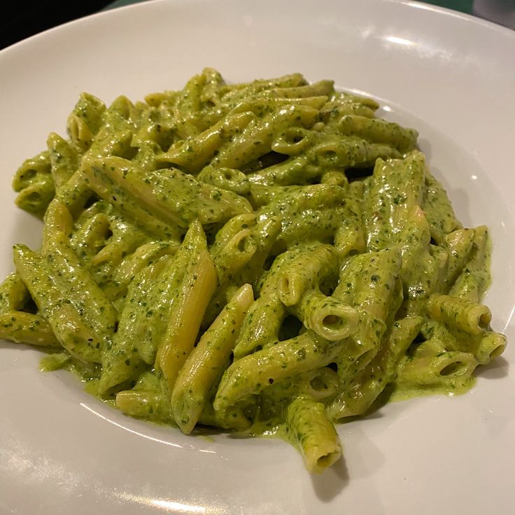 a white plate topped with green pasta covered in pesto