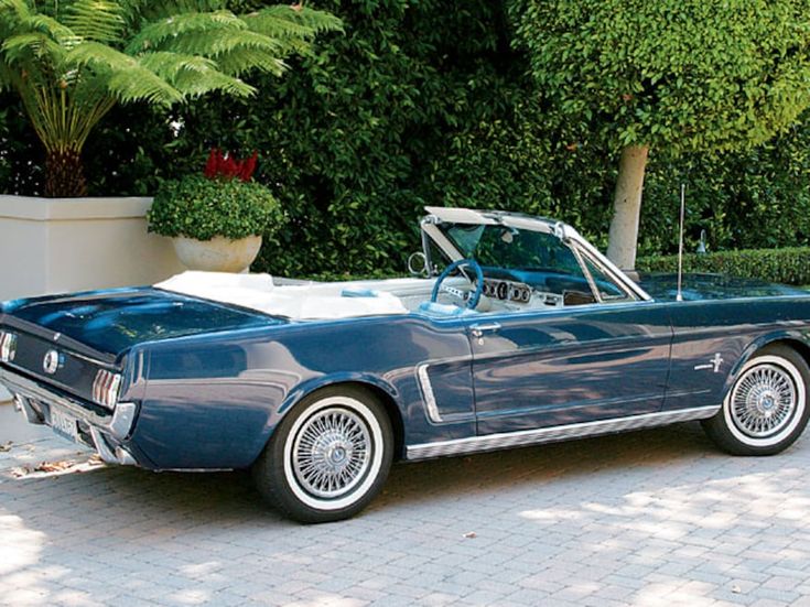 an old blue convertible car parked in front of a planter filled with potted plants