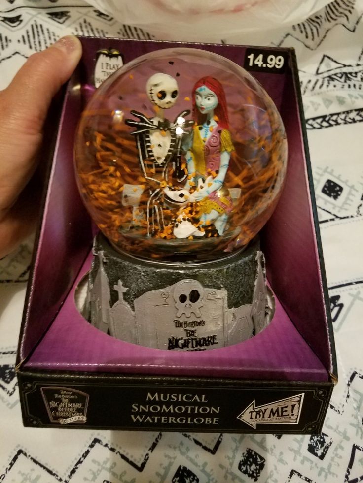 someone is holding a snow globe with skeletons in it on a bed and there are other items inside the box