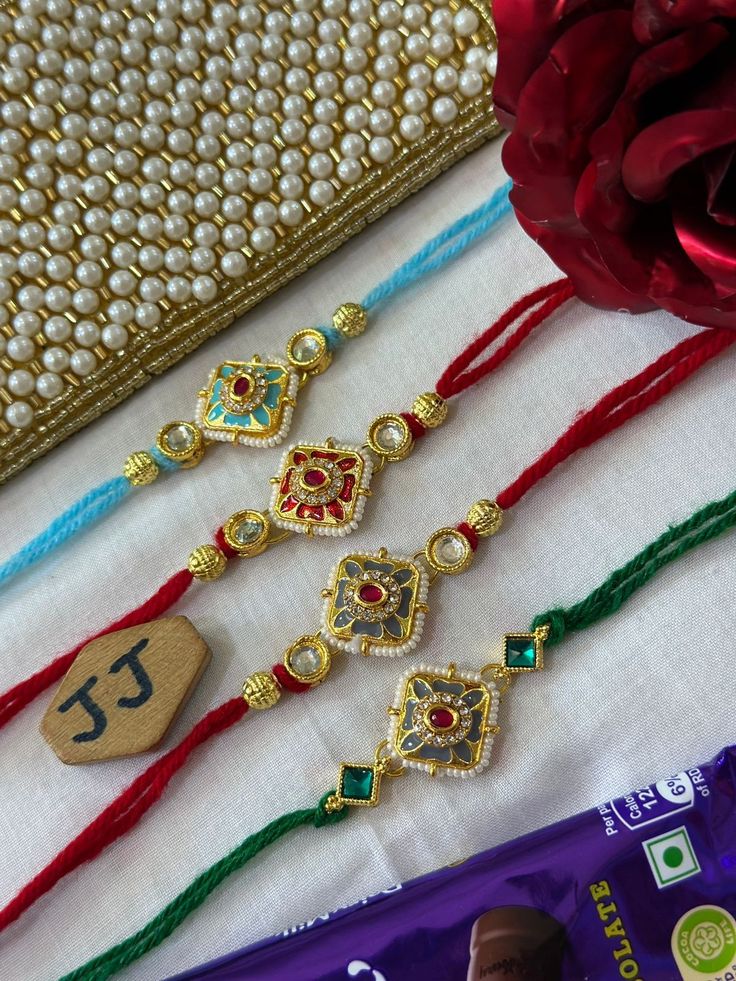 three rakholi with one red rose and the other two green, gold - plated beads