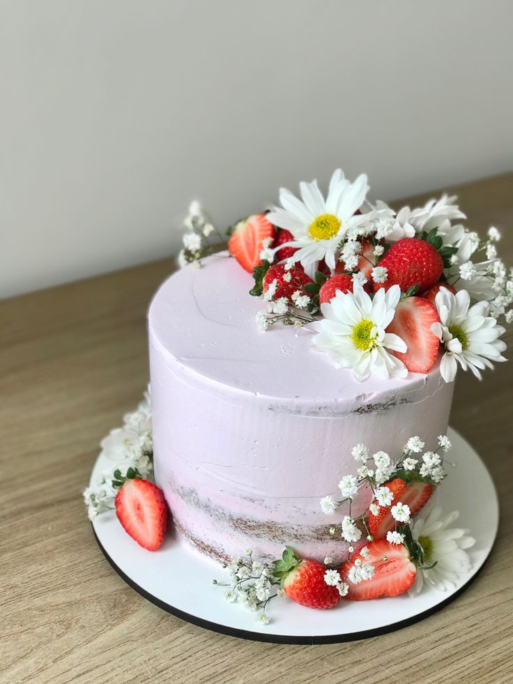 a white cake with strawberries and daisies on top sits on a wooden table