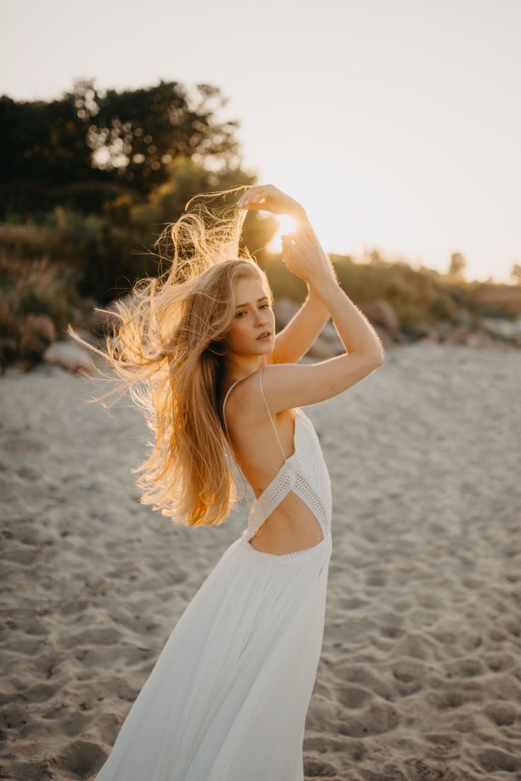 a woman standing on top of a sandy beach holding her hair in front of the sun