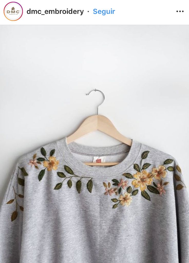 a gray sweater with flowers on it hanging from a hanger in front of a white wall