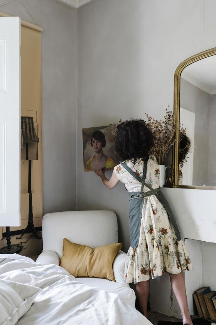 a woman standing in front of a mirror on top of a bed next to a white couch