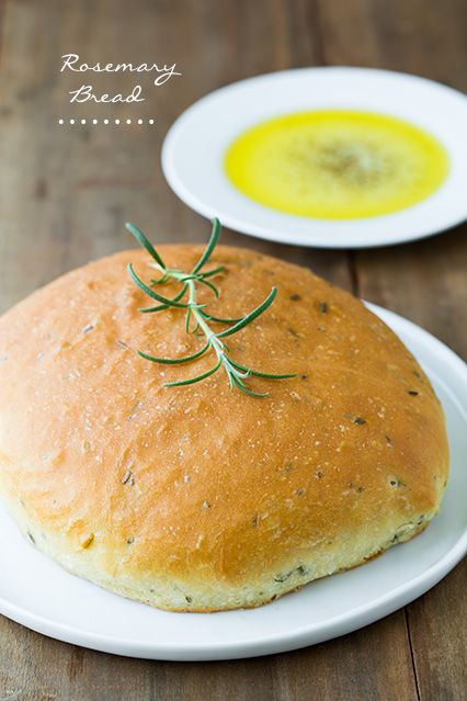 bread with rosemary on top sitting on a white plate next to a bowl of olive oil