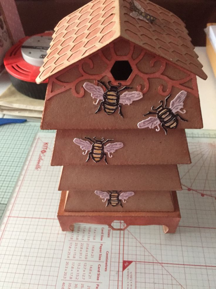 a birdhouse with bees on it sitting on top of a piece of paper next to a ruler