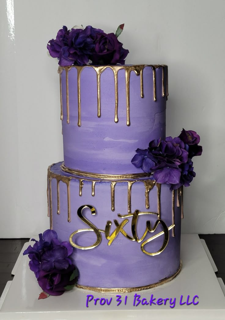 a three tiered cake with purple flowers and dripping icing on the top layer