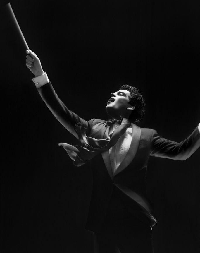 a black and white photo of a man in a tuxedo holding a baton