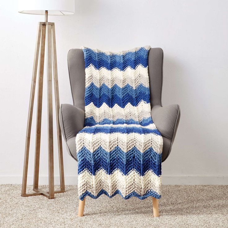 a blue and white blanket sitting on top of a chair next to a lamp in a room