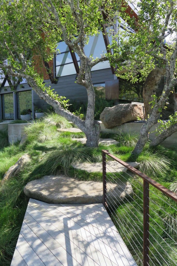 a wooden walkway in front of a house with trees and grass on the side walk