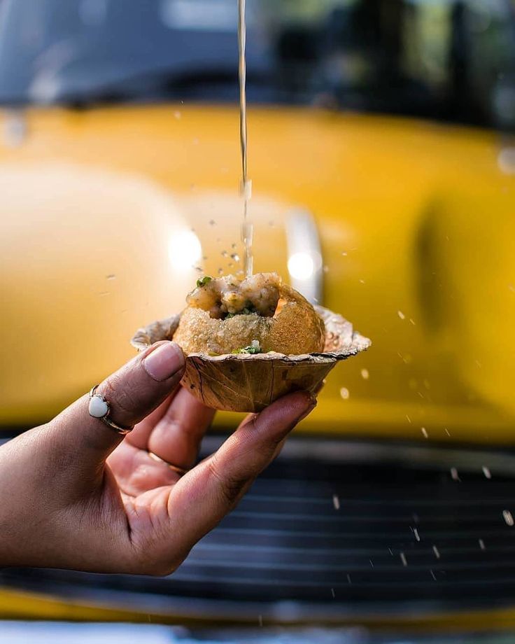 a person is holding food in front of a yellow car with water pouring out of it