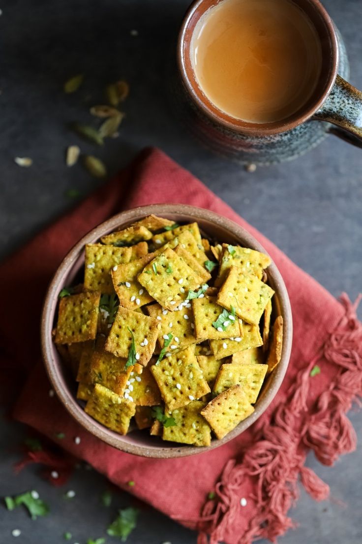 a bowl filled with crackers next to a cup of tea on top of a red napkin