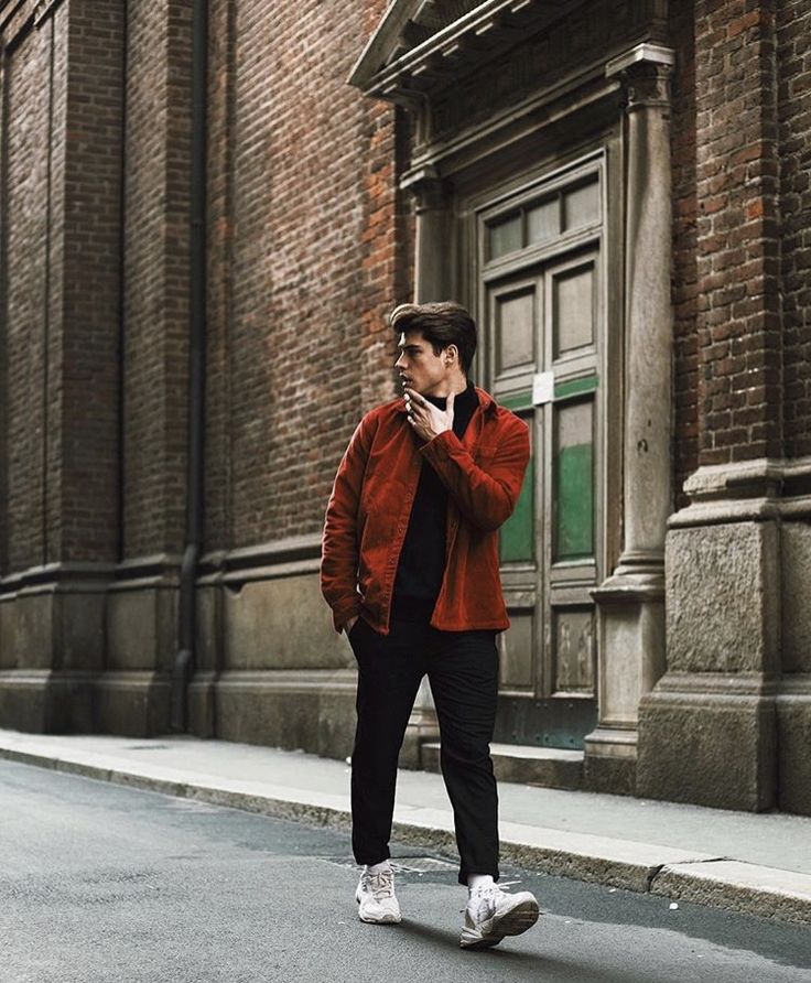 a man is walking down the street while talking on his cell phone and wearing an orange jacket