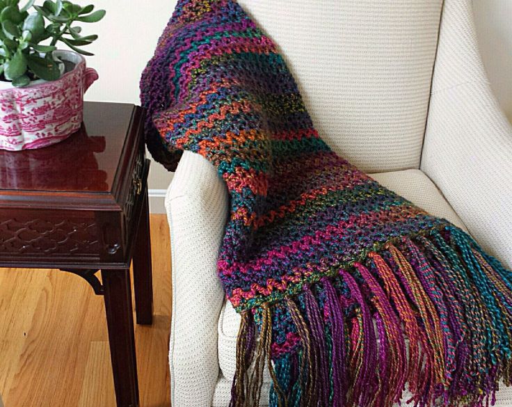 a crocheted blanket sitting on top of a chair next to a potted plant