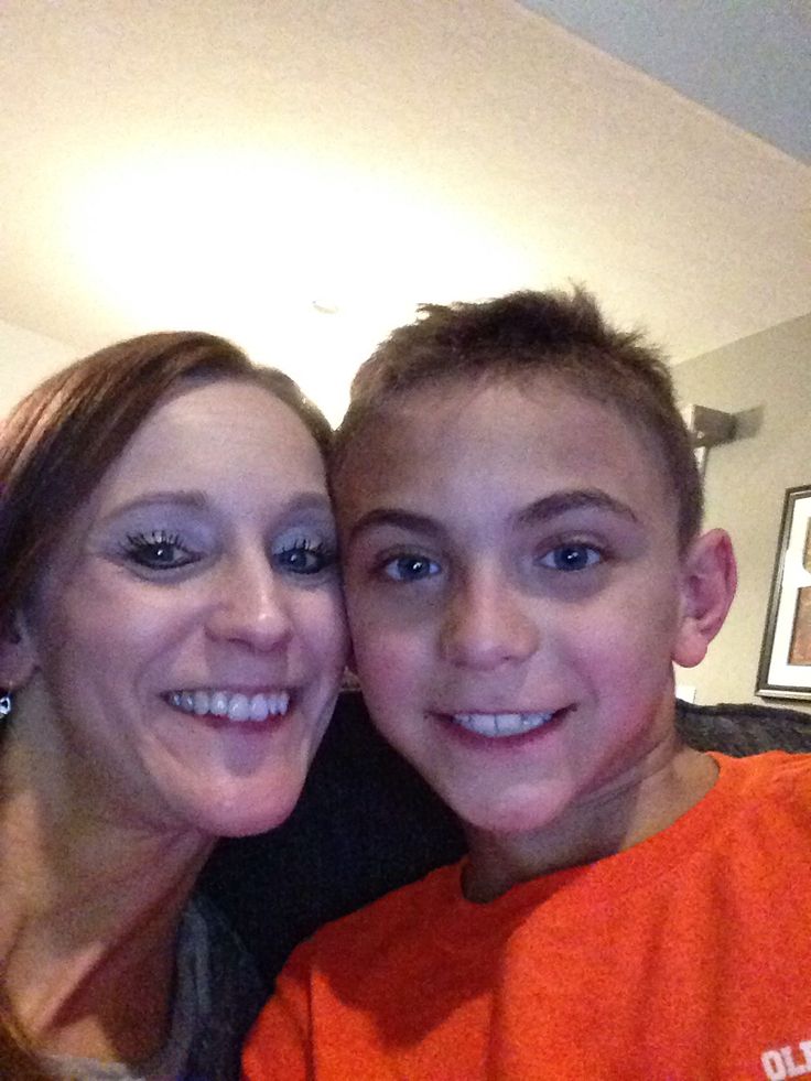 a woman standing next to a young boy in front of a tv screen and smiling at the camera