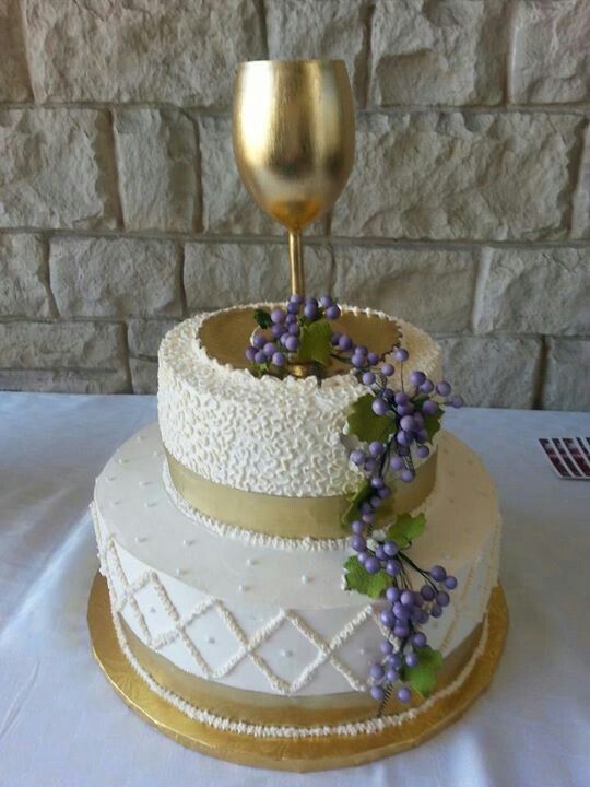 a three tiered wedding cake with purple flowers on the side and a gold wine goblet