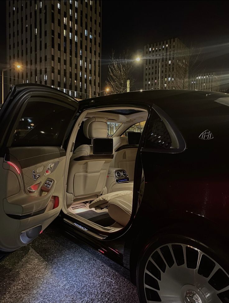 the interior of a car with its door open at night in front of tall buildings