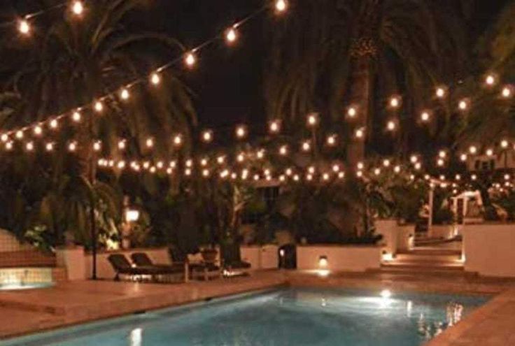 an outdoor swimming pool with lights strung over it