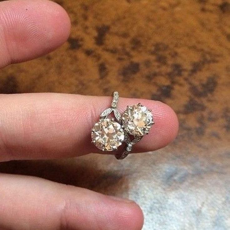 a person's hand holding an engagement ring with two diamonds on top of it