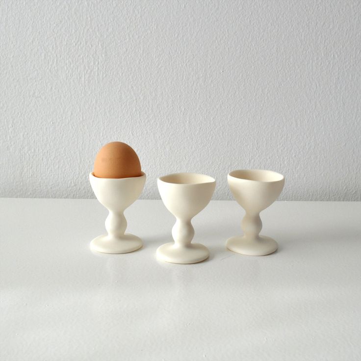 three egg cups sitting on top of a table next to an egg in the middle