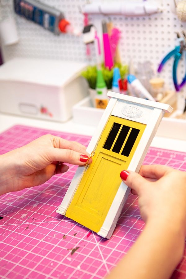 a woman is making a doll house out of cardboard and plastic material with her hands