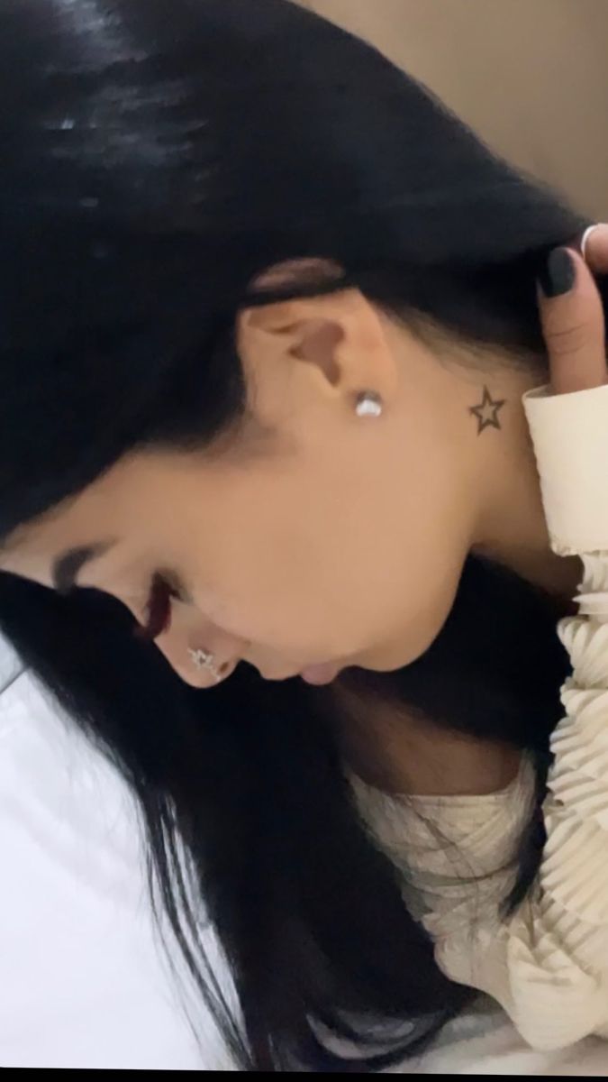 a woman with long black hair and piercings on her ear wearing a white shirt