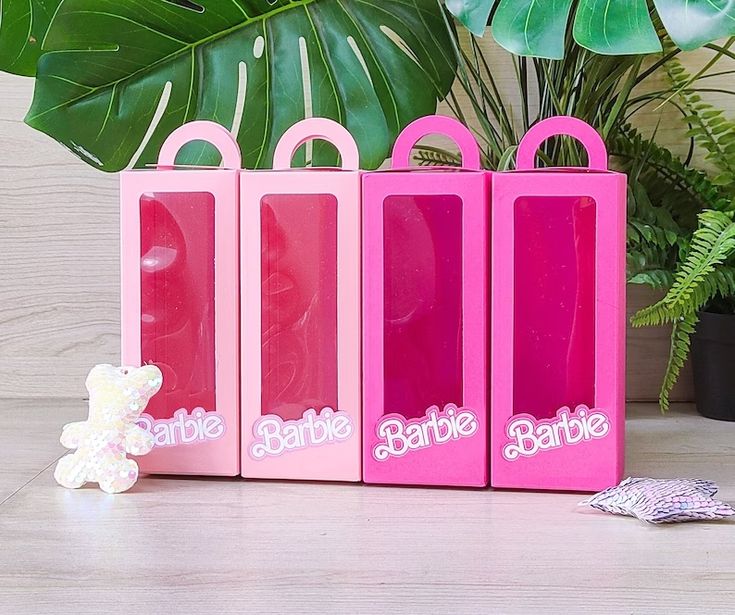 three pink bags sitting on top of a table next to a teddy bear and potted plant