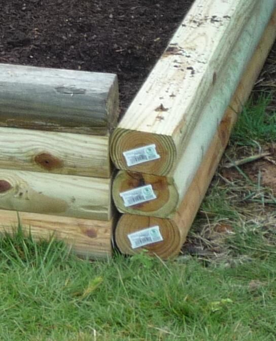 two logs stacked on top of each other in the grass near some dirt and mulch