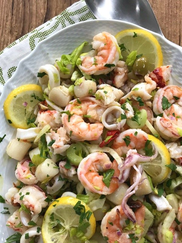 a white bowl filled with shrimp salad and lemon wedges on top of a wooden table