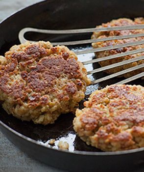 two hamburger patties being cooked in a skillet with tongs on the side