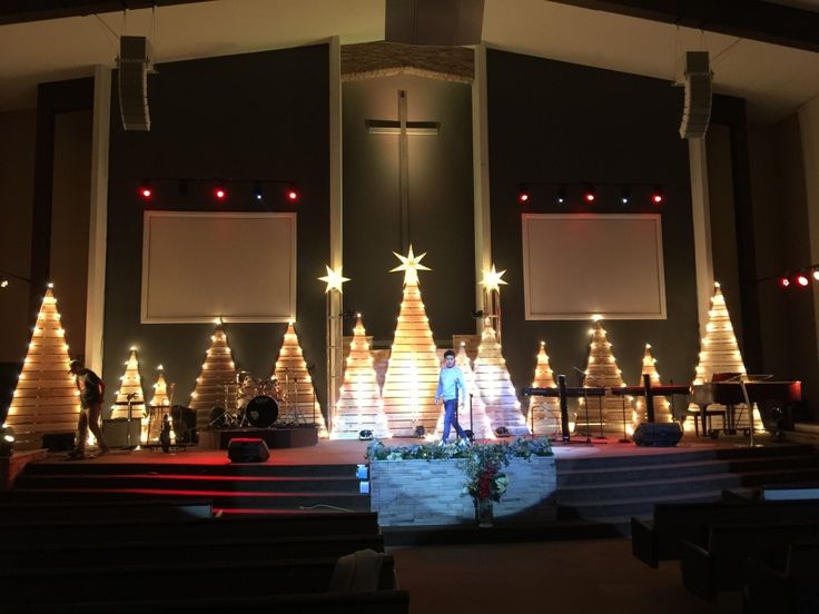 a man standing in front of a church with christmas trees on the stage and lights all around him