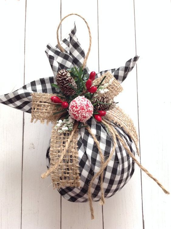 a christmas ornament hanging on the side of a white wooden wall with pine cones and berries