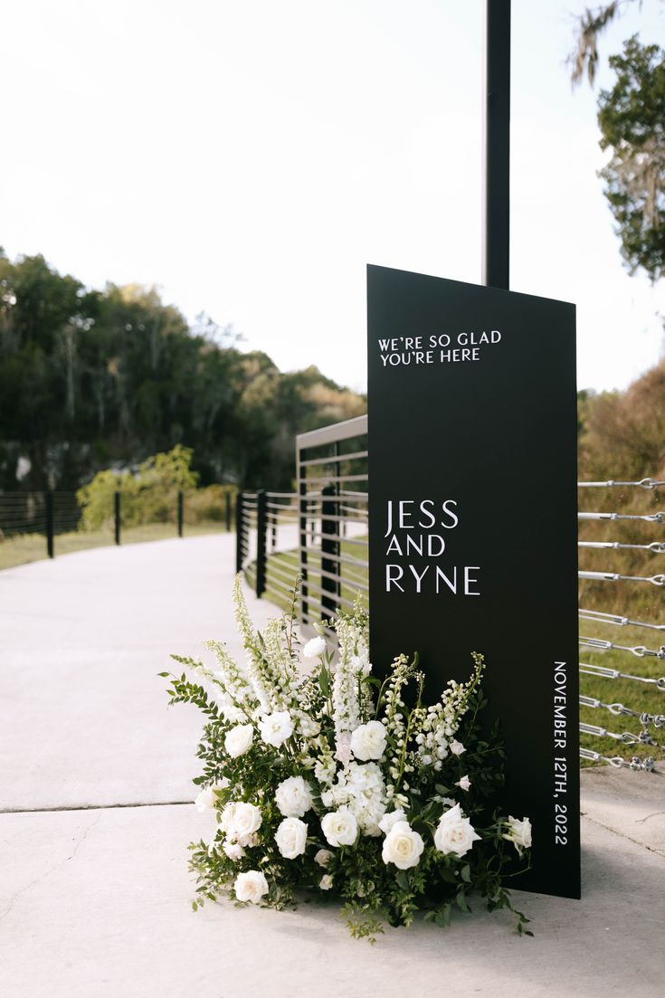 white flowers and greenery are placed in front of a sign