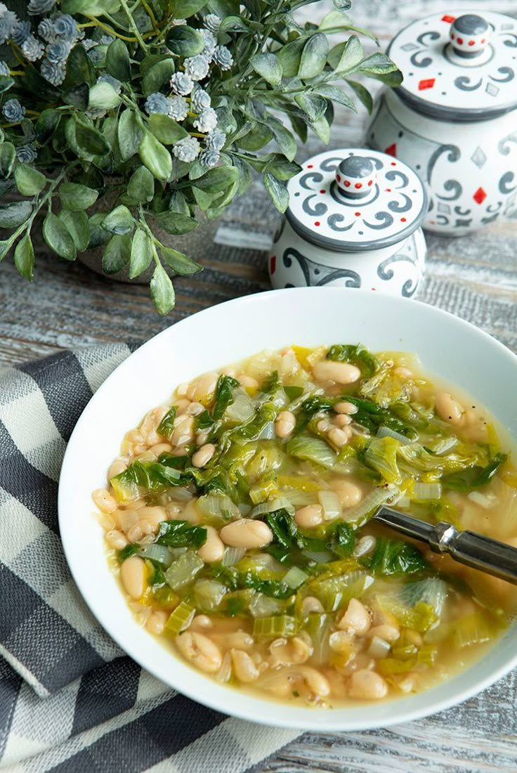 a white bowl filled with beans and greens on top of a checkered table cloth