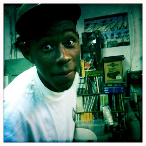 a man with a hat on in front of a book shelf