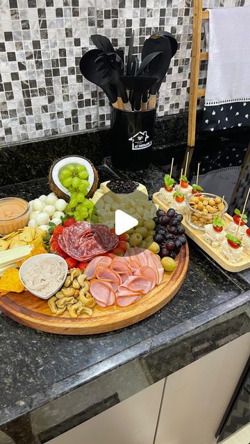 a platter of cheeses, meats and fruit on a kitchen counter with utensils