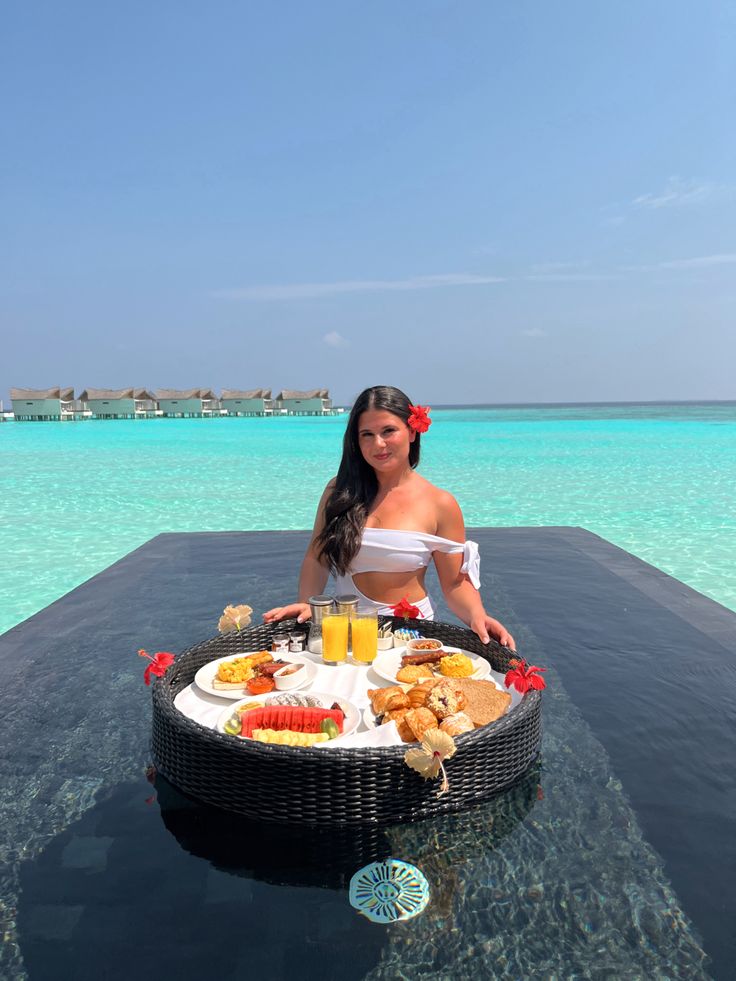 a woman sitting at a table with food on it in the middle of an ocean