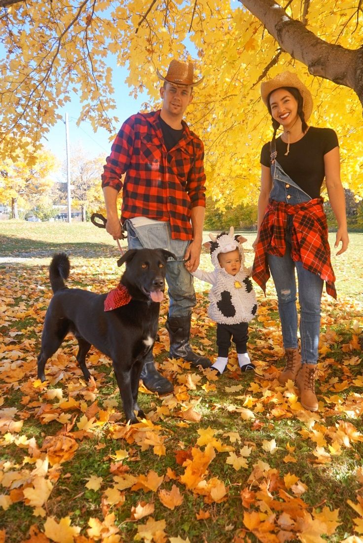 a man, woman and child are standing under a tree with their dog in the fall leaves