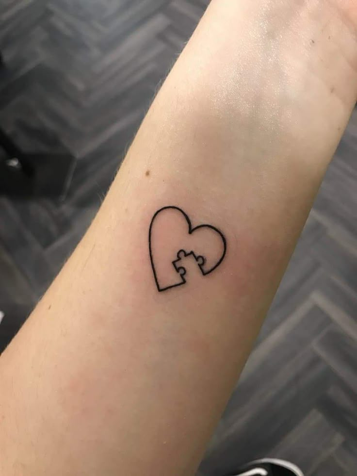 a small heart shaped puzzle tattoo on the wrist