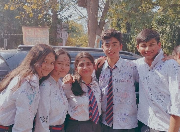 a group of young people standing next to each other in front of a parked car