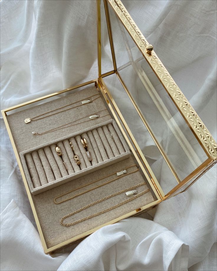 an open jewelry box on a bed with white sheets in the background and gold jewelry inside