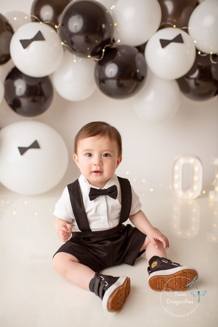 a baby sitting on the floor in front of some balloons and wearing a bow tie